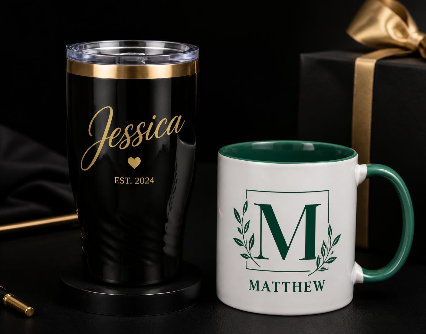 Personalized black tumbler with gold script lettering beside a white mug with a green monogram